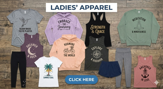 A collection of women’s apparel arranged on a rustic wooden floor, featuring a lavender "Embrace the Journey" hoodie, black "Strength & Grace" tank, grey leggings, and a salmon "Anchored in Love" tank